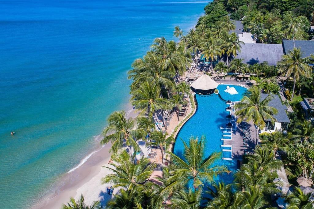 Tropu kūrorts ar tropiskiem kokiem un zilo baseinu, kas atrodas tuvumā pie pludmales un okeāna. Ideāla vieta atpūtai un relaksācijai.