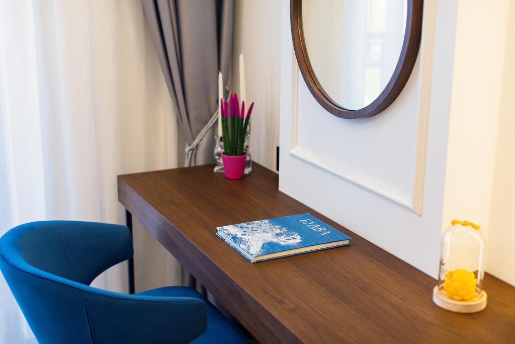 Mūsdienīgs rakstāmgalds ar zilā krāsā krēslu, dekorēts ar augu, grāmatu un spoguli, radot elegantu un mājīgu atmosfēru.