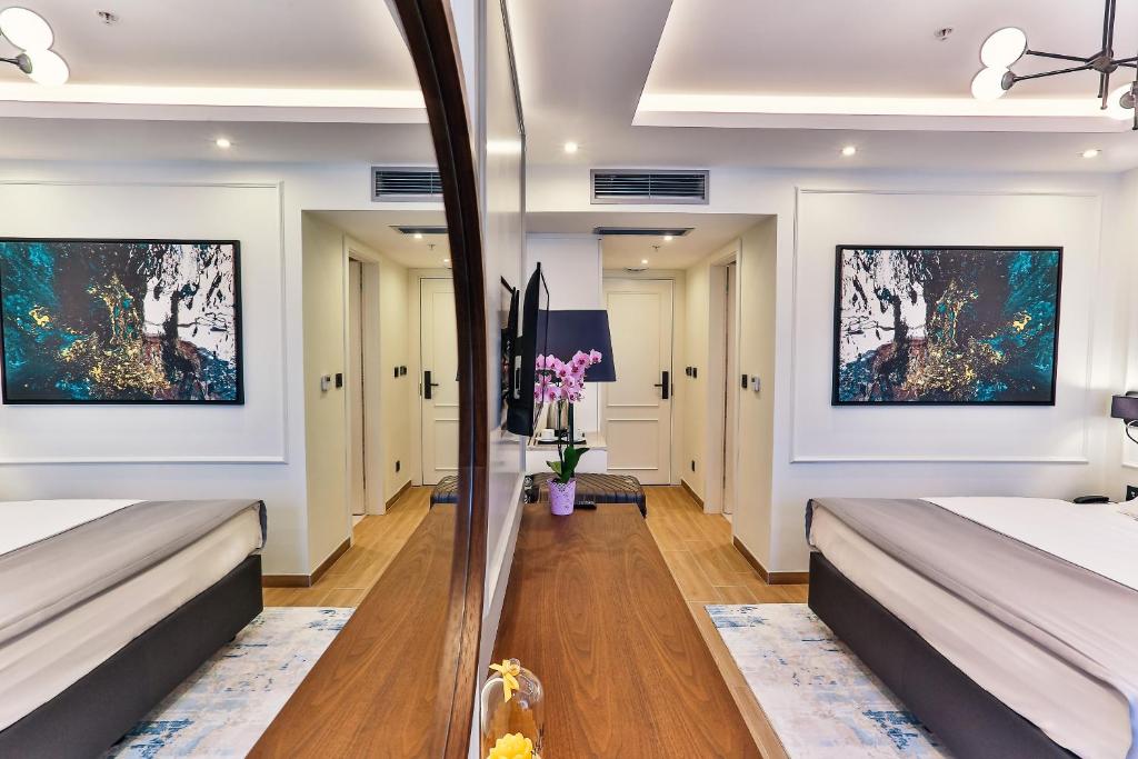 Mūsdienīgs viesnīcas numurs ar elegantu interjeru, kurā ir liela spoguļpaneļa daļa, mākslas darbs uz sienas un ziedi uz galda. Numurā ir gaismas un koka elementi, radot siltu un viesmīlīgu atmosfēru.