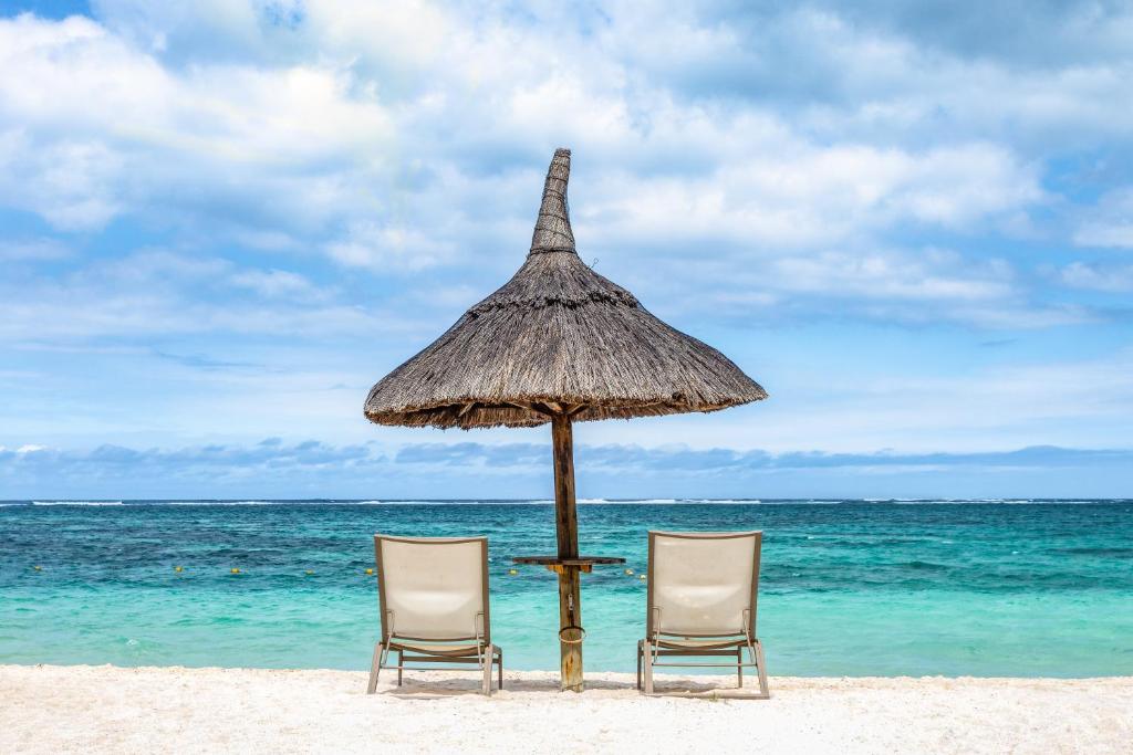 Divi pludmales krēsli zem salmu jumtiņa, skatoties uz mierīgu okeāna ainavu ar zilu debesu fonu.