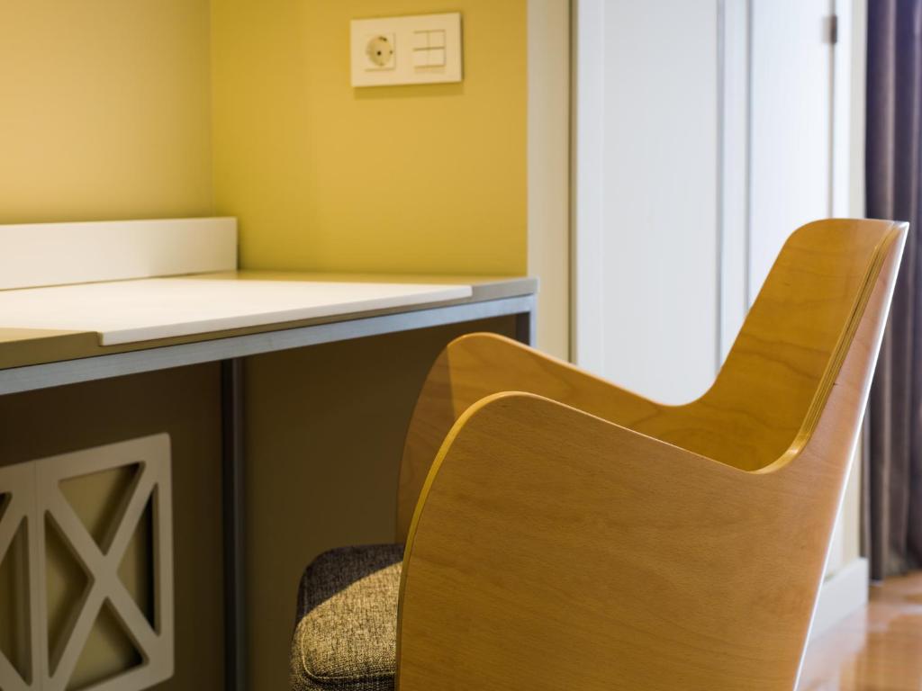 Mūsdienīgs rakstāmgalds ar koka krēslu, kas atrodas gaišā telpā. Dzeltenā siena un elektrības kontaktligzda pie galda piešķir telpai siltu un mājīgu atmosfēru.