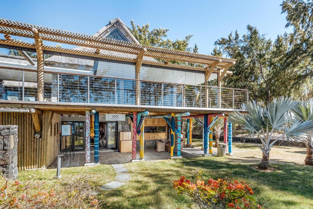 Mūsdienīga ēka ar koka konstrukciju un krāsainiem stabiem, kas atrodas zaļā vidē. Terase ar stikla barjeru nodrošina skatu uz apkārtni.