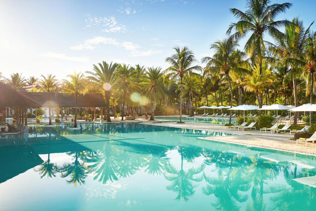 Tropu viesnīcas baseins ar palmām un saulainu debesīm, radot relaksējošu atmosfēru. Ideāla vieta atpūtai un baudīšanai.