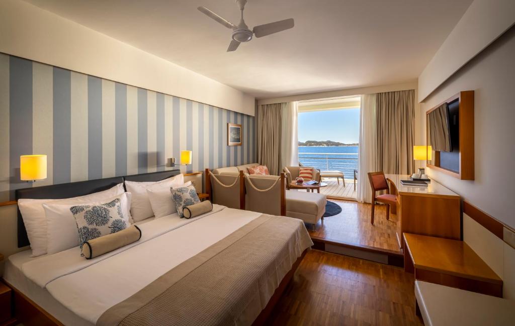 Grezns viesnīcas numurs ar skatu uz jūru, kurā ir divguļamā gulta, komfortabla atpūtas zona un lieli logi, kas ļauj ienākt dabiskajai gaismai.