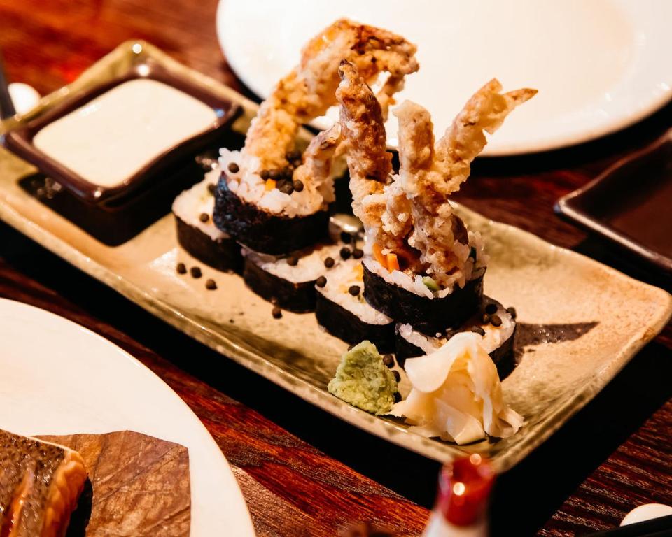 Svaigu sushi rullīši ar kraukšķīgām garnelēm, pasniegti uz keramikas šķīvja kopā ar mērci un wasabi.
