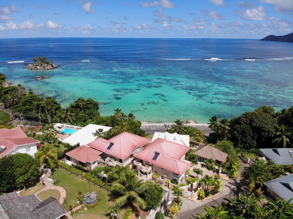 Skaista ainava ar skaidru zilo ūdeni un tropu ainavu, kur redzami māju jumti un peldbaseins pie krasta.