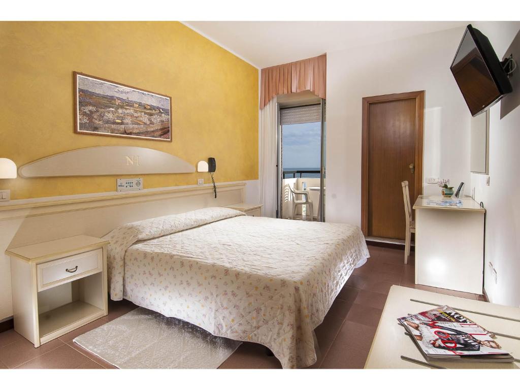 Mūsdienīga viesnīcas numura iekārtojums ar divguļamo gultu, dīvānu un rakstāmgaldu. Pirmajā plānā redzama glezna uz dzeltenas sienas, logā ir skats uz jūru.