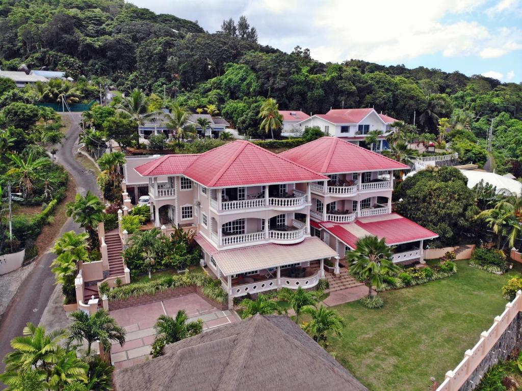 Trīsstāvu māja ar sarkanu jumtu, ieskauta zaļiem kokiem un zālienu, atrodas kalnu apvidū. Apkārt mājai ir labi kopti dārzi un ceļi, kas ved uz apkārtējām ēkām.