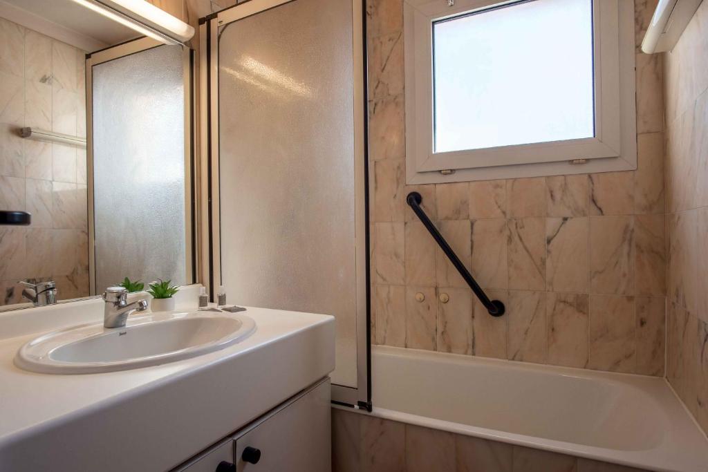 Moderns vannas istabas interjers ar baltu izskatu un dabīgu apgaismojumu. Tajā ir vanna, izlietne un spogulis, kā arī dekoratīvs augs uz izlietnes.