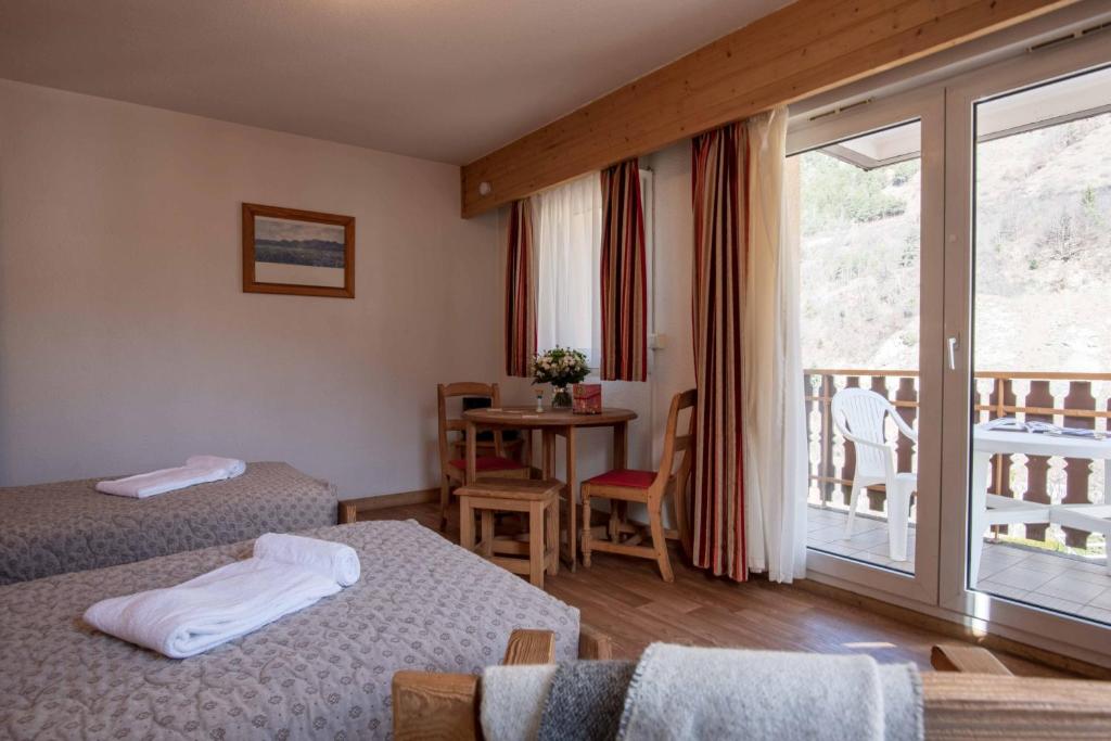 Gaiša viesnīcas numura iekārtojums ar divām gultām un galdu, kas ir blakus balkona durvīm. Numurā redzami koka elementi un dabiska apgaismojuma ietekme.