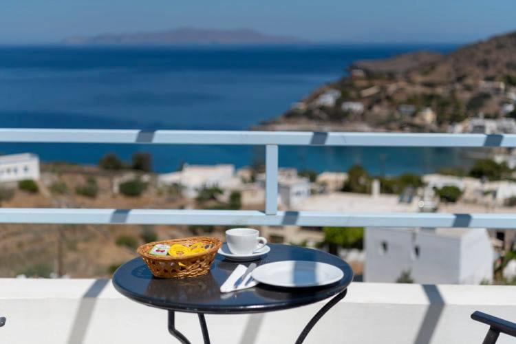 Balkona galdiņš ar kafijas krūzi un maizes grozu, redzama jūra un apkārtējā ainava.