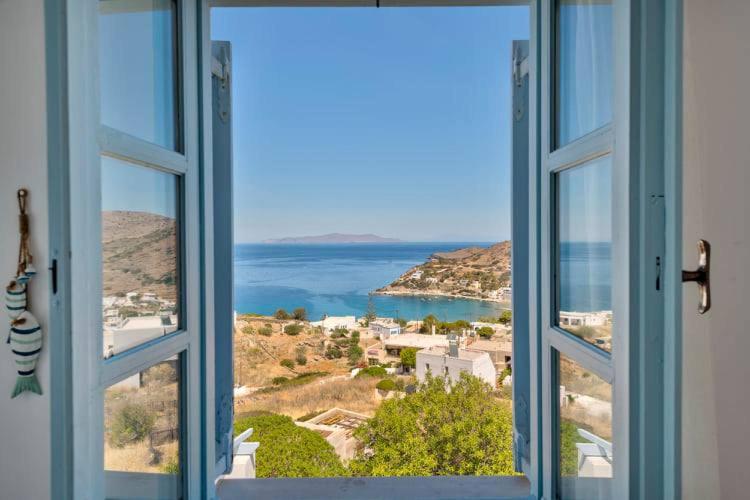 Skats no loga uz jūras ainavu, kur var redzēt kalnainu krastu un mierīgu ūdeni. Apkārtējā vide ir saulaina un mierīga, radot relaksējošu atmosfēru.