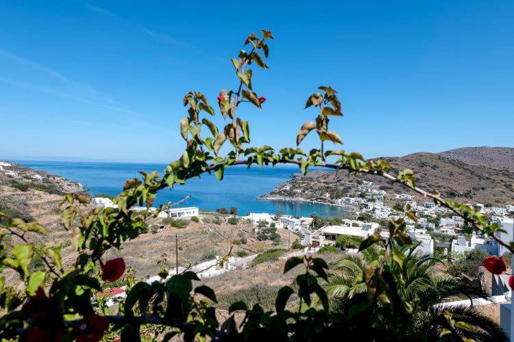 Skats uz jūru ar zaļiem augiem priekšplānā un kalnu ainavu fona. Saules gaisma izgaismo apdzīvotas vietas piekrastē.