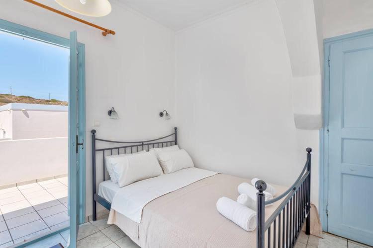 Maza, gaiša guļamistaba ar divguļamo gultu, tīrām baltām sienām un zilu durvju rāmīti, kas ved uz terasi. Gultai pievienoti dvieļi un blakus sienās ir gaismas avoti.