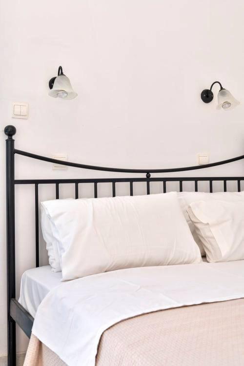 Vienkāršs gultas izskats ar melnu metāla rāmi un baltām gultas veļām, blakus esošas sienas lampas pie sienas.