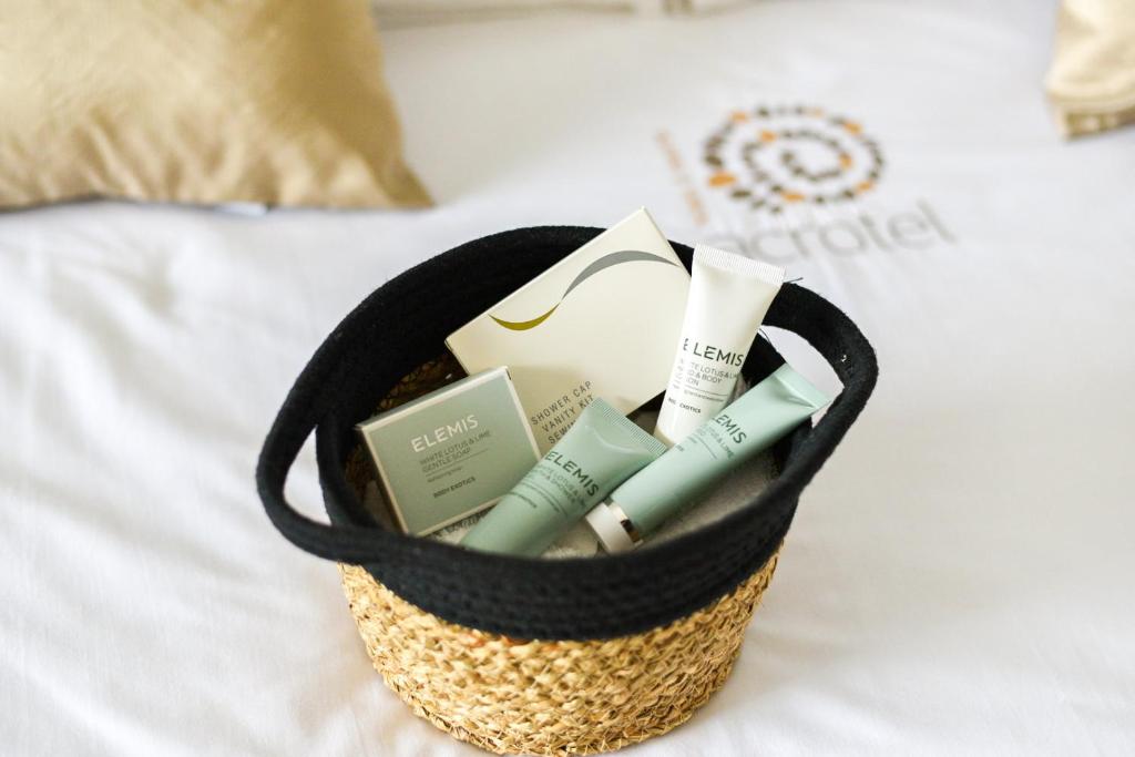 Maza groziņa ar ELEMIS ādas kopšanas produktiem, ieskaitot krēmus un sejas maskas, novietota uz gultas.
