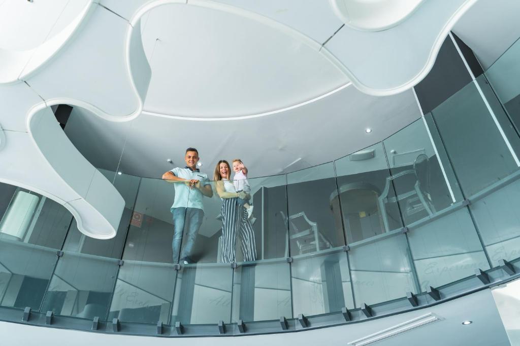 Skaista ģimene, kas stāv stikla balkona malā modernā interjerā, baudot laiku kopā. Gaisīga un moderna atmosfēra.