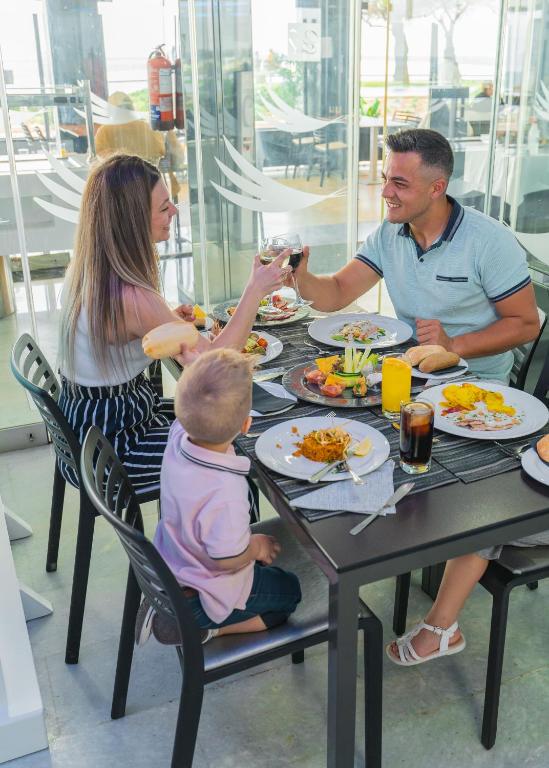 Ģimene izbauda maltīti modernā restorānā, satiekoties ap ēdamgaldu un daloties priekā un dzērienos. Uz galda ir dažādi ēdieni un dzērieni, kas veicina patīkamu atmosfēru.