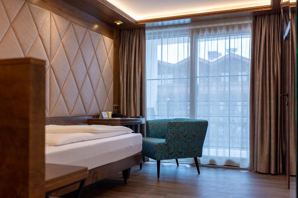 Eleganta viesnīcas istaba ar modernu dizainu, kurā ir gultas, stilīgs krēsls un lieli logi ar aizkariem. Istaba izceļas ar siltām krāsām un komfortablu atmosfēru.