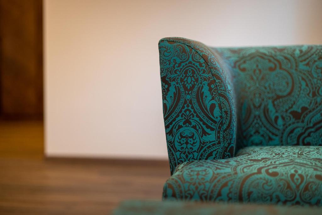 Teal krāsas dīvāna stūris ar rakstainu audumu, kas izceļas uz neitrālas krāsas fona.
