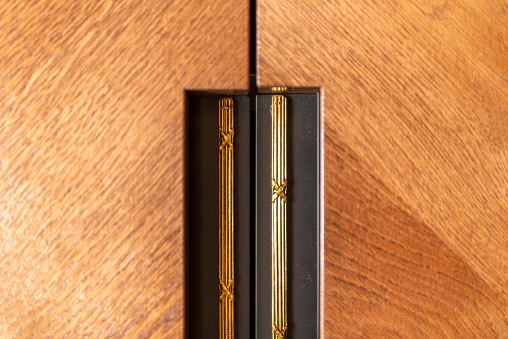 Koka durvju rokturis ar zeltītiem elementiem, kas piešķir eleganci un stilu. Roktura forma un tekstūra izceļas uz koka virsmas.