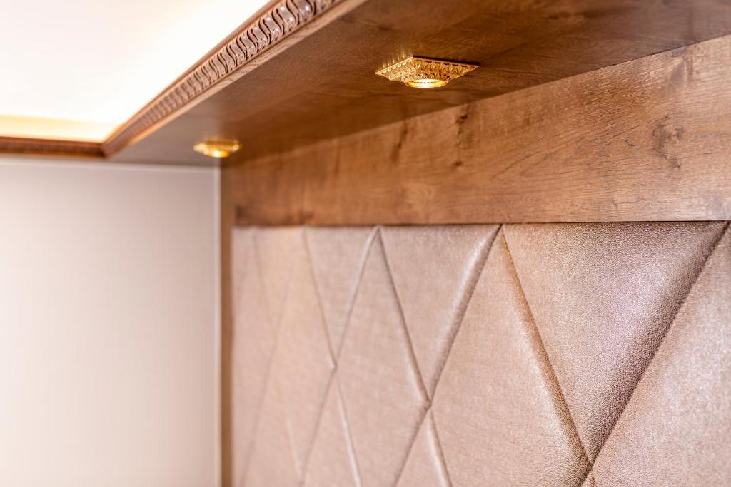 Elegantā interjera detaļa ar koka apdari un mīksto audumu, kas veidots ar dimanta formas rakstu. Uzsvars uz gaismas avotiem un tekstūras kontrastu.