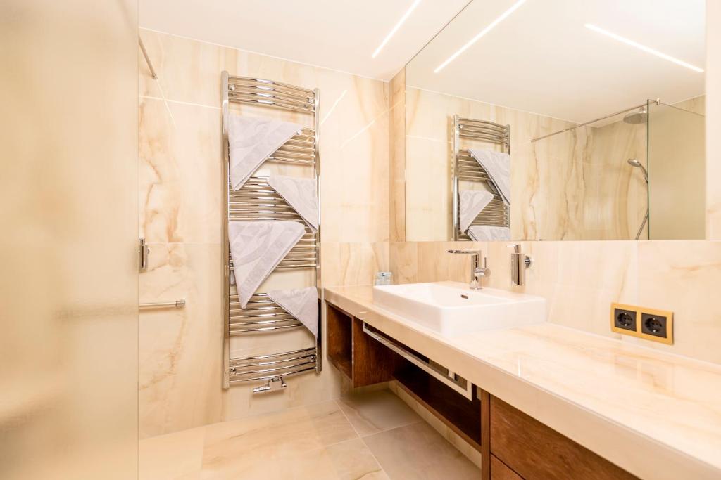 Mūsdienīga vannas istaba ar elegantu dizainu, kurā ir gaismas paneļi, stilīgs izlietnes pults un hromēts dvieļu žāvētājs. Sienas ir klātas ar smalku akmens izskatu, radot nomierinošu atmosfēru.