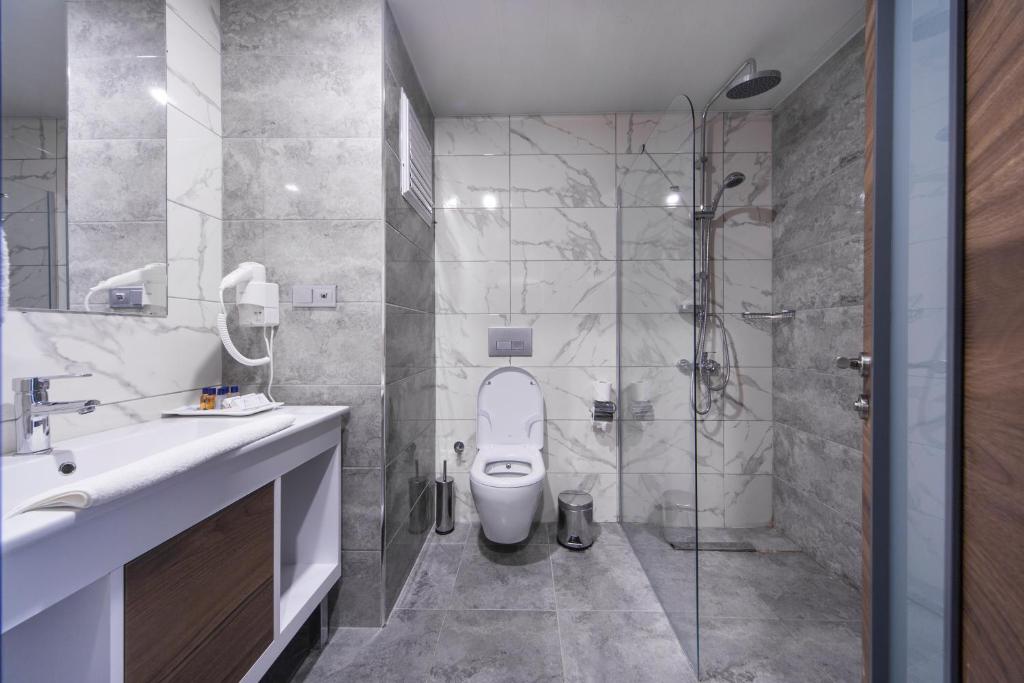 Mūsdienīgs un elegants vannas istabas interjers ar stikla dušu, pelēku flīžu apdari un minimālistisku dizainu. Ideāls piemērs komfortablai un stilīgai telpai.