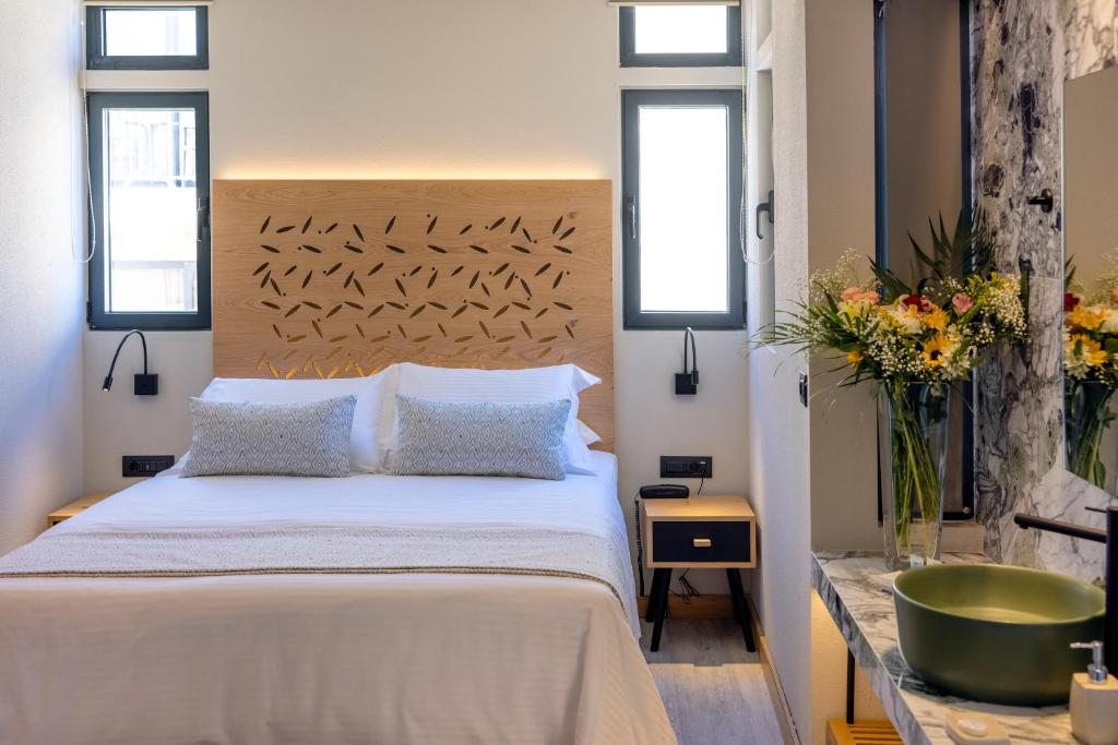 Mūsdienīgs guļamistabas interjers ar koka gultas galvgali un ziedu kompozīciju. Viegla gaisma un eleganta dizaina elementi rada patīkamu atmosfēru.