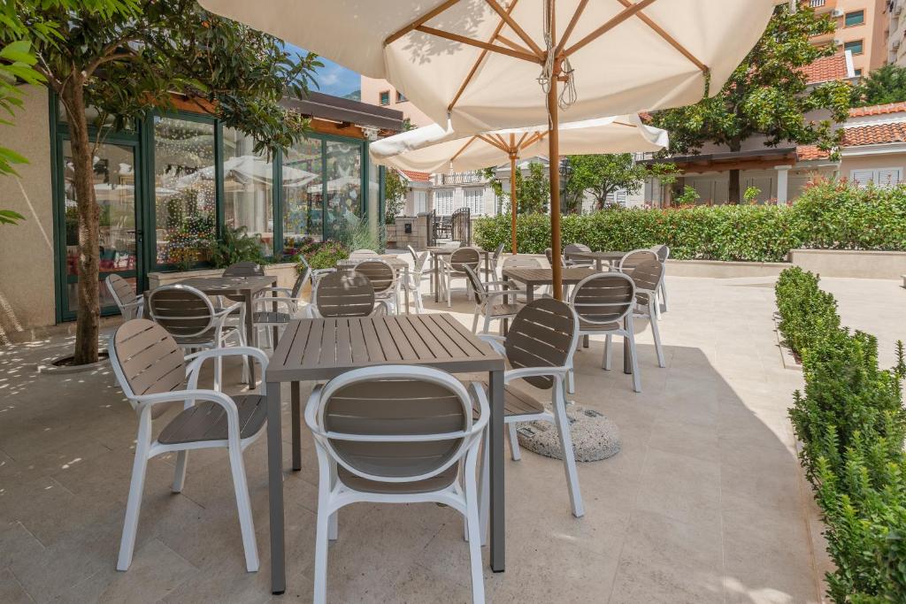 Āra kafejnīcas terase ar moderniem galdiem un krēsliem, pārklāta ar saulessargiem, apstādīta ar zaļumiem un kokiem. Ideāla vieta relaksācijai un ēdiena baudīšanai.