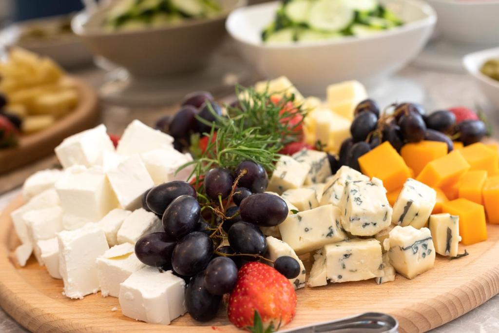 Siera un augļu plate ar dažādiem sieriem, melnajiem vīnogām un zemenēm, kas rotā koka griešanas dēli. Ideāla uzkoda svinībām vai kopā sanākšanai.