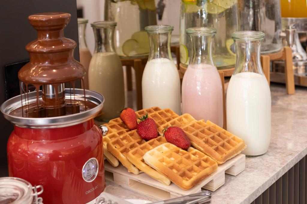 Šokolādes strūklaka ar vafelēm un zemenēm, blakus atrodas pudeles ar pienu un jogurtu.