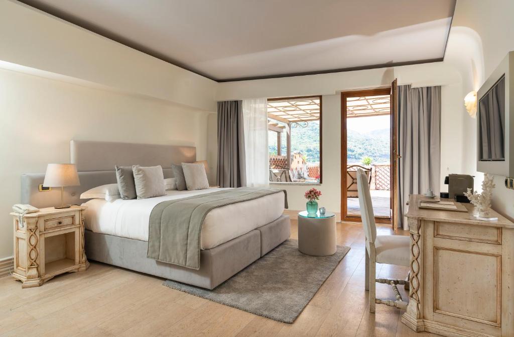 Mūsdienīga guļamistaba ar lielu gultu, koka grīdu un piekļuvi balkonam ar skatu uz dabu. Telpā ir elegantas mēbeles un gaišas krāsas, radot komfortablu atmosfēru.