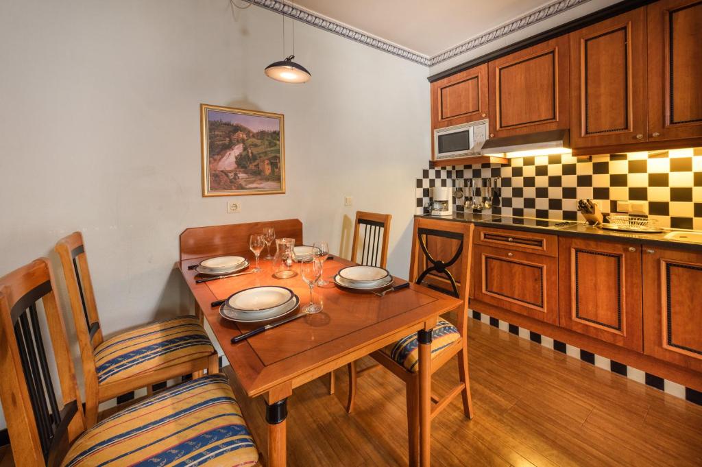 Kompakta un mājīga virtuve ar koka mēbelēm, galdu, kas uzklāts ar traukiem un glāzēm, un modernu virtuves tehniku. Ideāla vieta ēdiena gatavošanai un maltīšu baudīšanai.