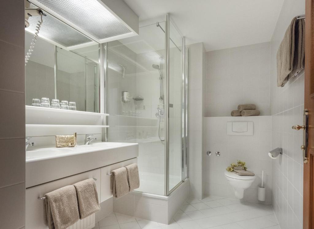 Mūsdienīgs, gaišs vannas istabas interjers ar stikla dušu, divām izlietnēm un elegantiem dvieļiem. Telpa ir aprīkota ar mūsdienīgām iekārtām un tīru, minimalistisku dizainu.