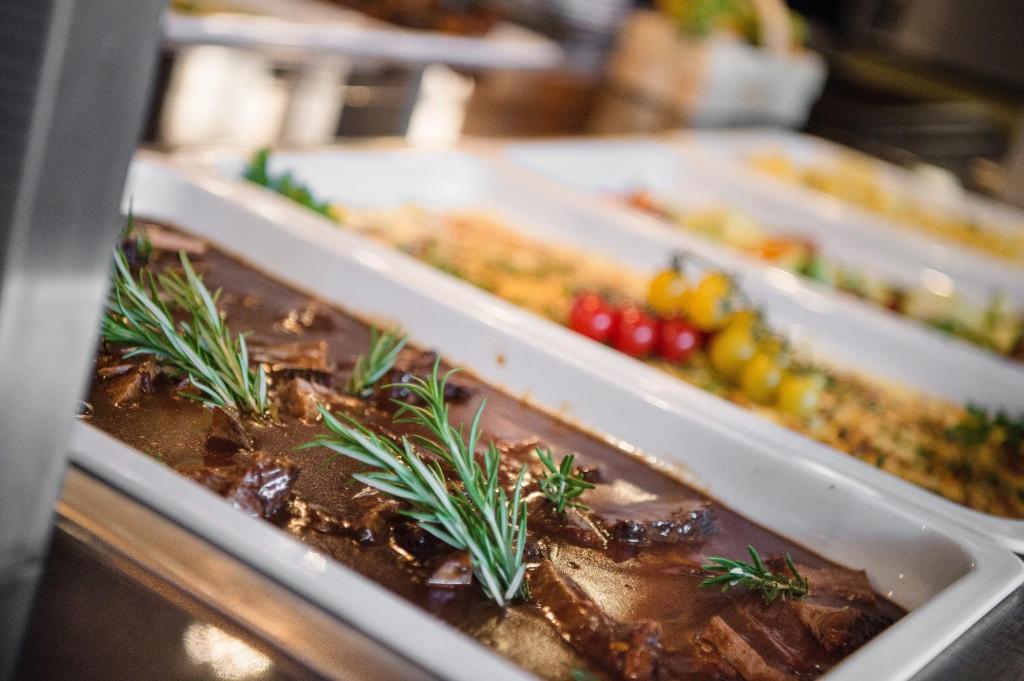 Gaļas ēdiens ar rozmarīnu un blakus esošajiem garnējumiem, kas pasniegti baltās traukos.