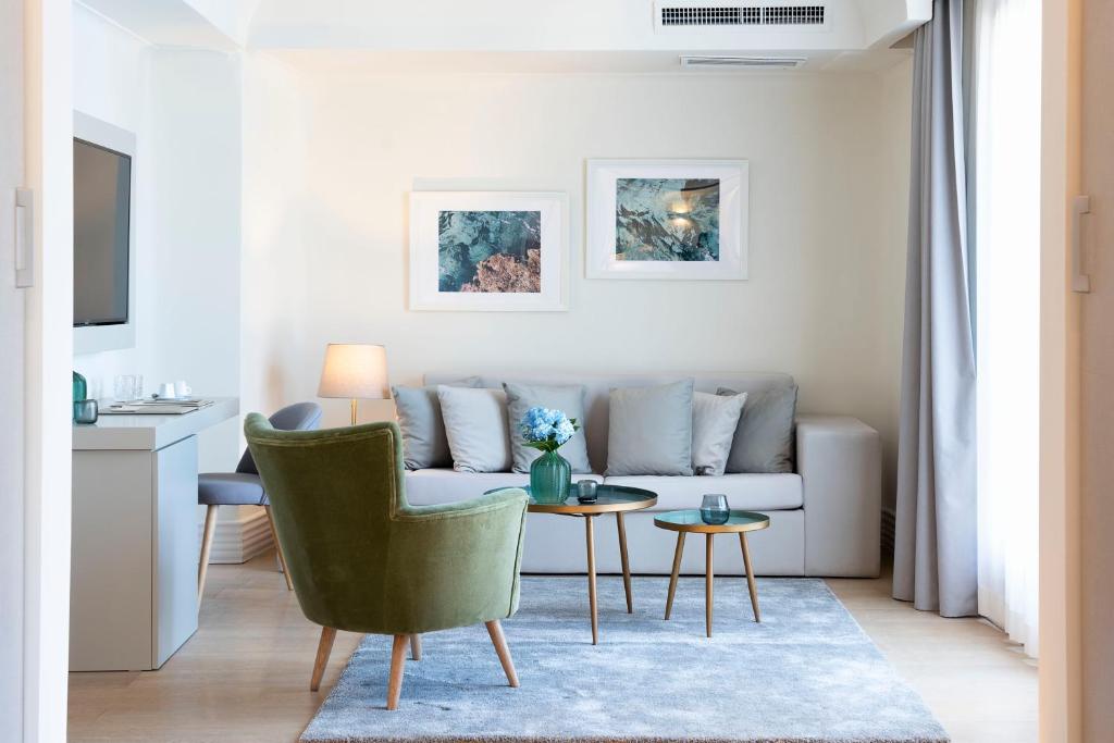 Mūsdienīgs viesistabas interjers ar zaļu krēslu, pelēku dīvānu un dekoratīvām gleznām uz sienām. Telpā ir arī nelieli galdiņi un aksesuāri, kas rada mājīgu atmosfēru.