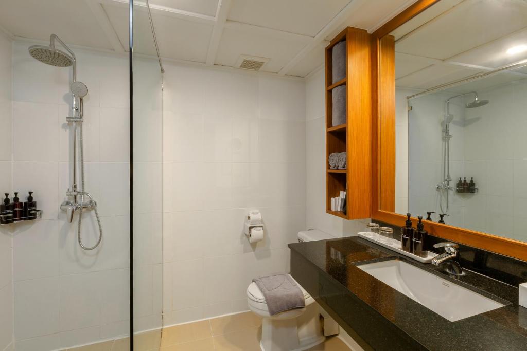 Mūsdienīgs vannas istabas interjers ar stikla dušu, tumša akmens izlietne un koka plaukti, kas satur dvieļus un higiēnas piederumus.