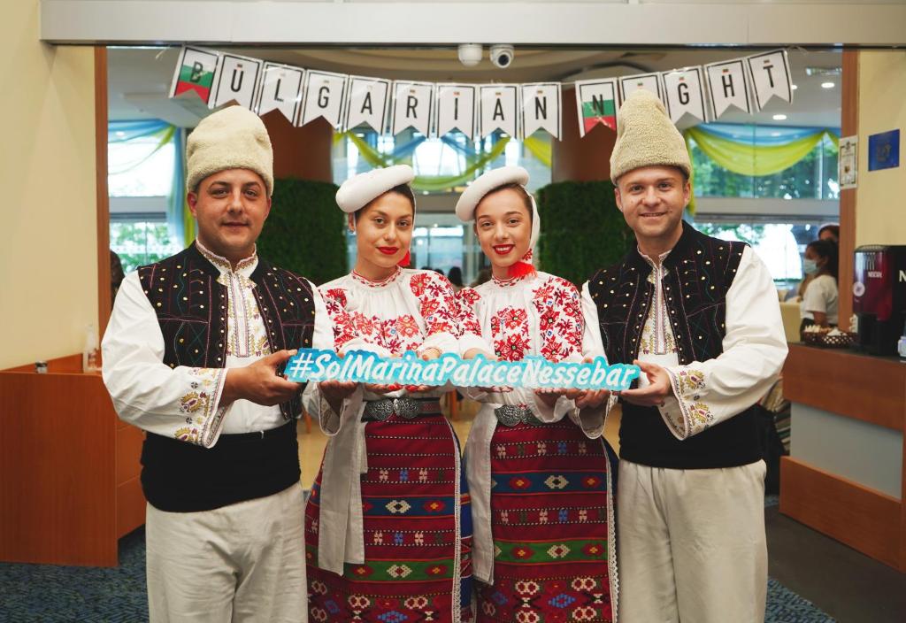 Tradicionālo bulgāru tērpu valkājoši dalībnieki pasākumā "Bulgāru nakts", turēdami zīmi ar hashtagu #SolMarinaPalaceNessebar.
