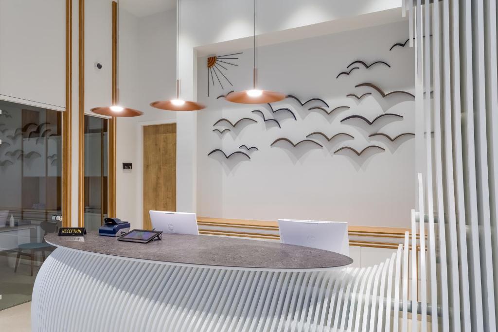 Mūsdienīga viesnīcas recepcija ar viļņveida dizainu, siltu apgaismojumu un stilizētām putnu figūrām uz sienas. Ideāla vide viesu uzņemšanai un relaksācijai.