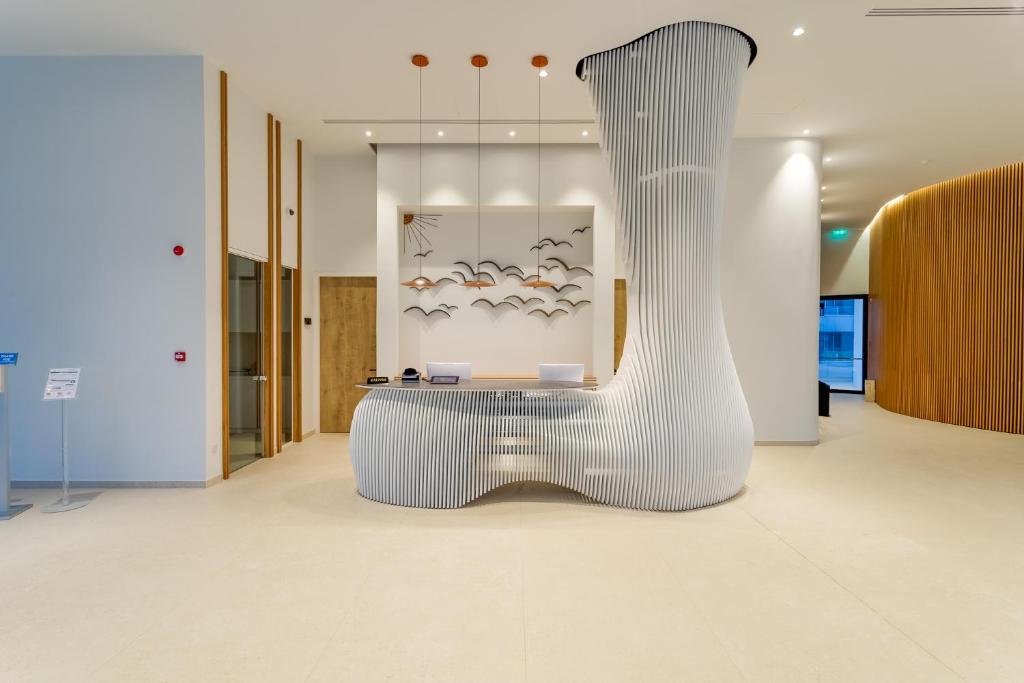 Mūsdienīga recepcija ar radošu dizainu, kas ietver viļņveidīgu galdu un māksliniecisku sienas dekoru. Telpa ir gaiša un plaša, radot viesmīlīgu atmosfēru.