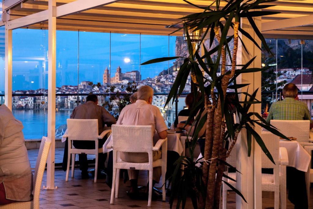 Elegantā restorāna skats ar viesiem, kas izbauda vakariņas, un gleznainu ainavu aiz loga, kas atspoguļo pilsētas gaismas.