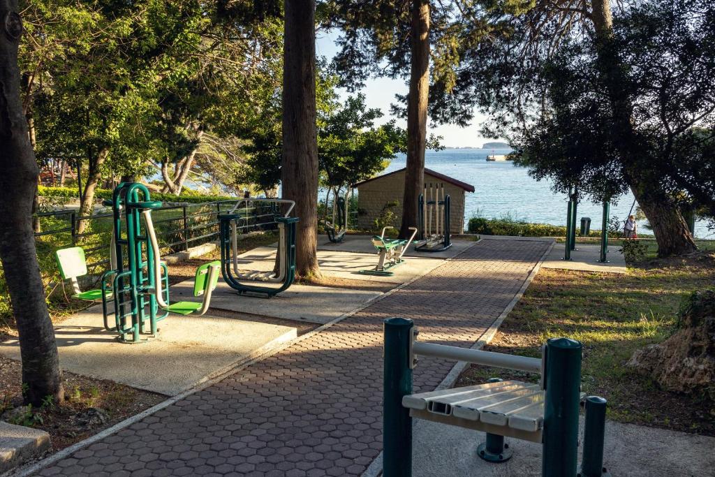 Āra sporta laukums ar trenažieriem un skatu uz jūru, ieskauts kokiem un zaļumiem. Ideāla vieta veselīga dzīvesveida aktivitātēm.