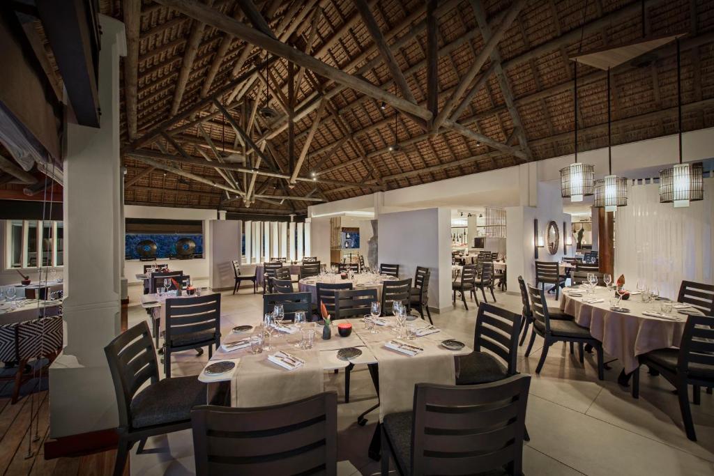 Mūsdienīgs restorāns ar augstiem koka griestiem un elegantiem galdiem, kas sagatavoti vakariņām. Interjers apvieno dabiskos materiālus un modernu dizainu, radot patīkamu atmosfēru.