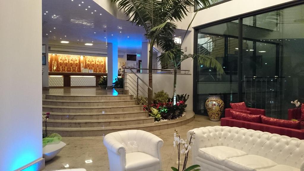 Mūsdienīgs viesnīcas vestibils ar elegantiem dīvāniem, apstādījumiem un apgaismojumu, kas rada viesmīlīgu atmosfēru. Redzama recepcija un kāpnes, kas ved uz augšējiem stāviem.