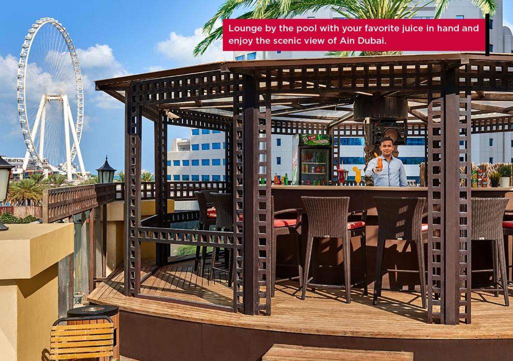 Atpūtas zona pie baseina ar dzērienu, kas tiek pasniegts bārā, un Ain Dubai skats fonā.