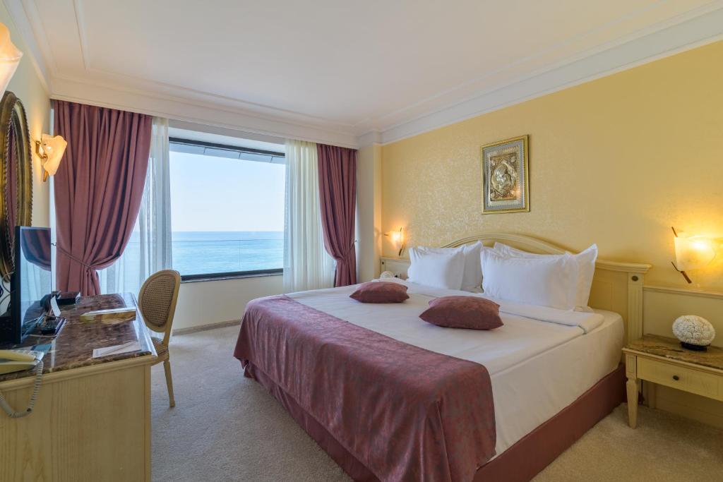 Labi iekārtota viesnīcas numuriņa interjers ar skatu uz jūru, ērts gultas komplekts un eleganti aizkari. Ideāli piemērots relaksējošai atpūtai.