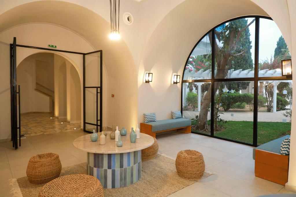 Mūsdienīgs viesnīcas interjers ar plašu logu, elegantām mēbelēm un relaksējošu atmosfēru. Dabiska gaisma un zaļumi radījuši patīkamu telpu atpūtai.