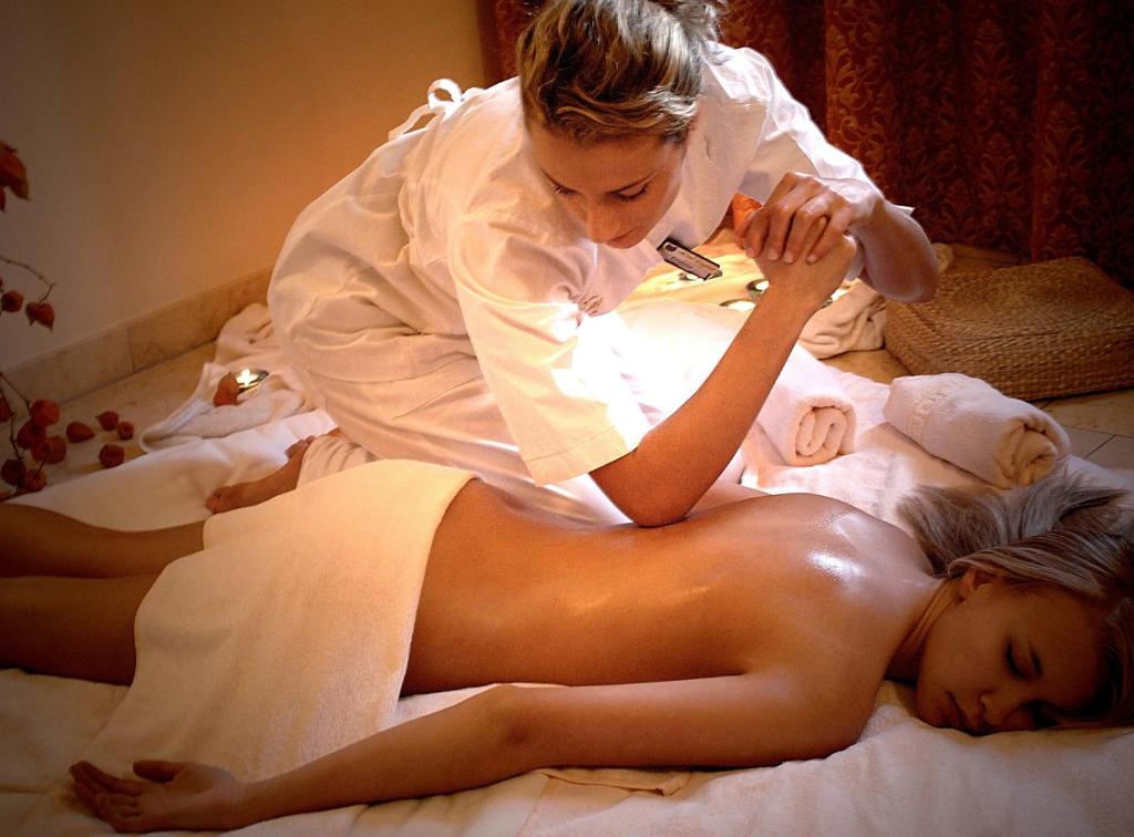 Masāžas sesija relaksējošā vidē, kur masieris veic masāžu uz guļoša klienta. Svaiga gaisotne ar mīkstām dvieļiem un siltu apgaismojumu.