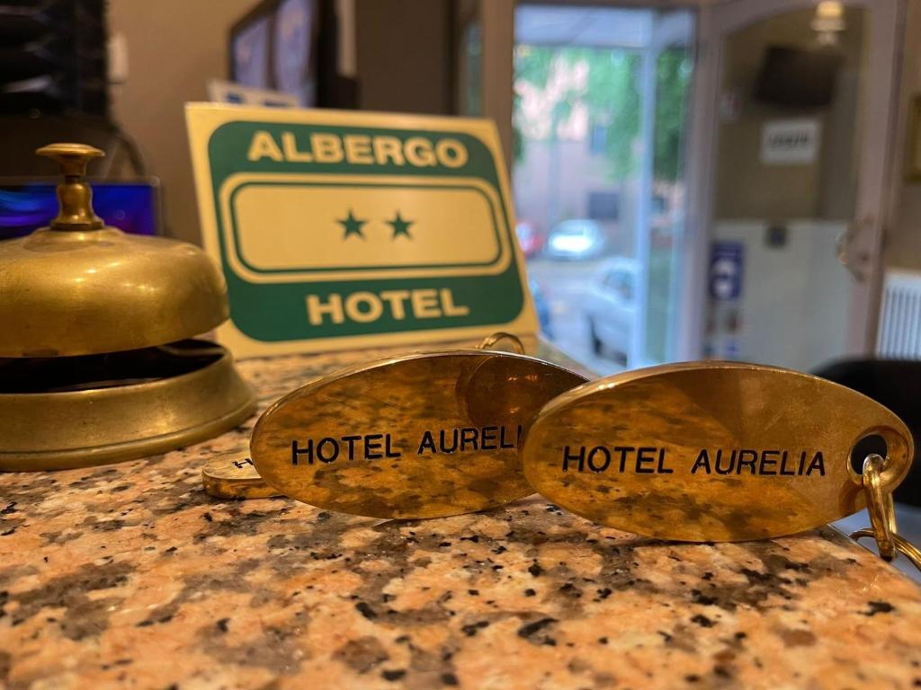 Reģistratūras skats ar viesnīcas zvanu un atslēgu piekariņiem "Hotel Aurelia", fonā redzama viesnīcas zīme.